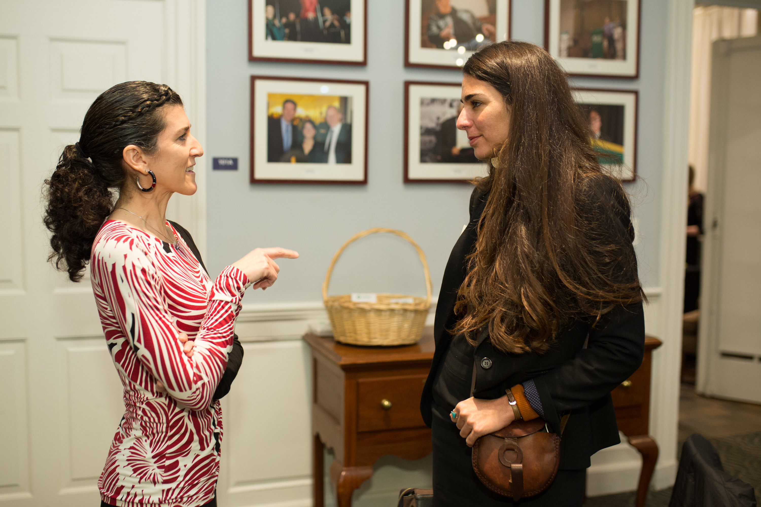 Lisa Fiore in a red and white dress stands and talks face-to-face with Saameh Solaimanim, who is dressed in black