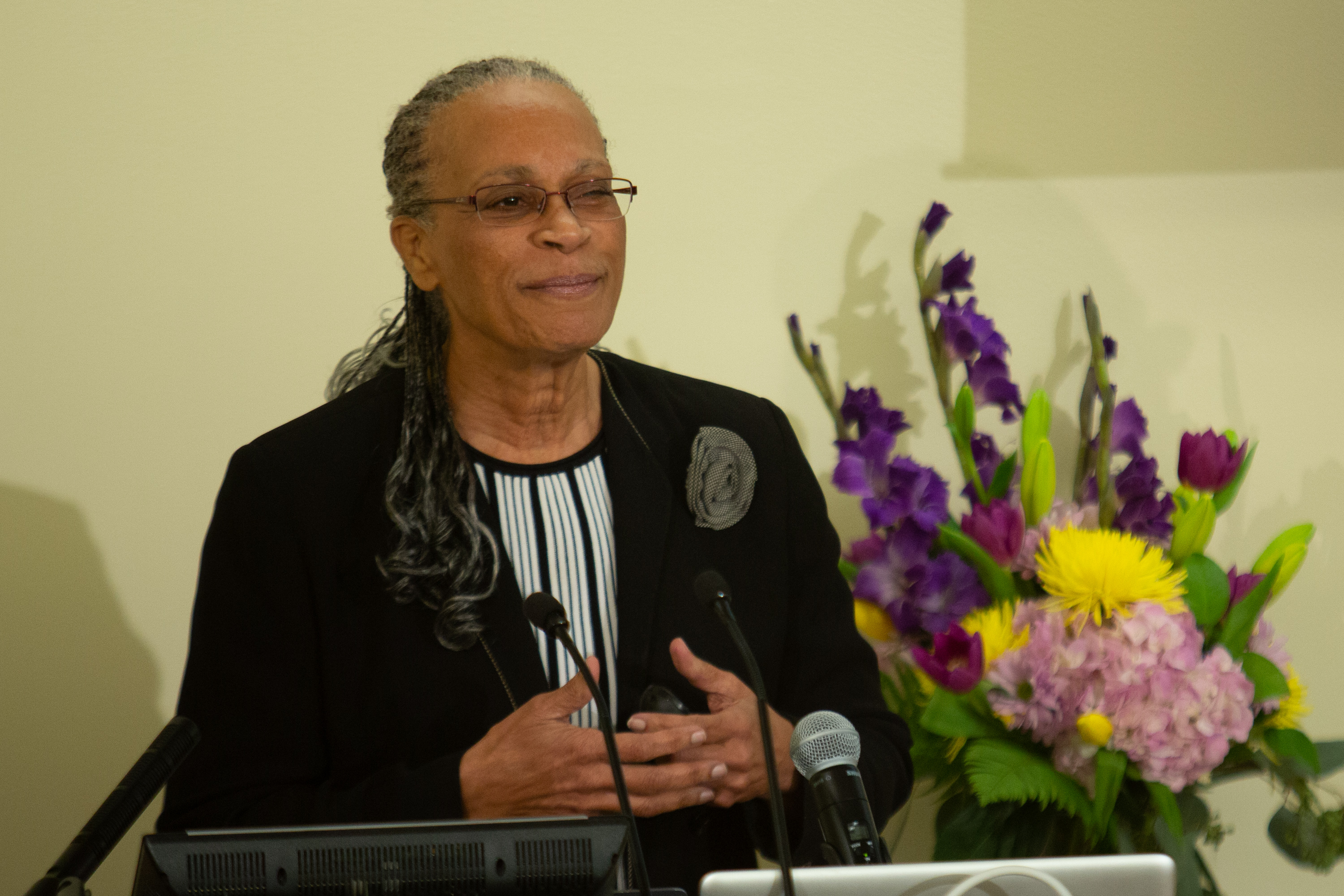 Dr. Arnetha Ball speaks at the podium with a bouquet of flowers in the background.