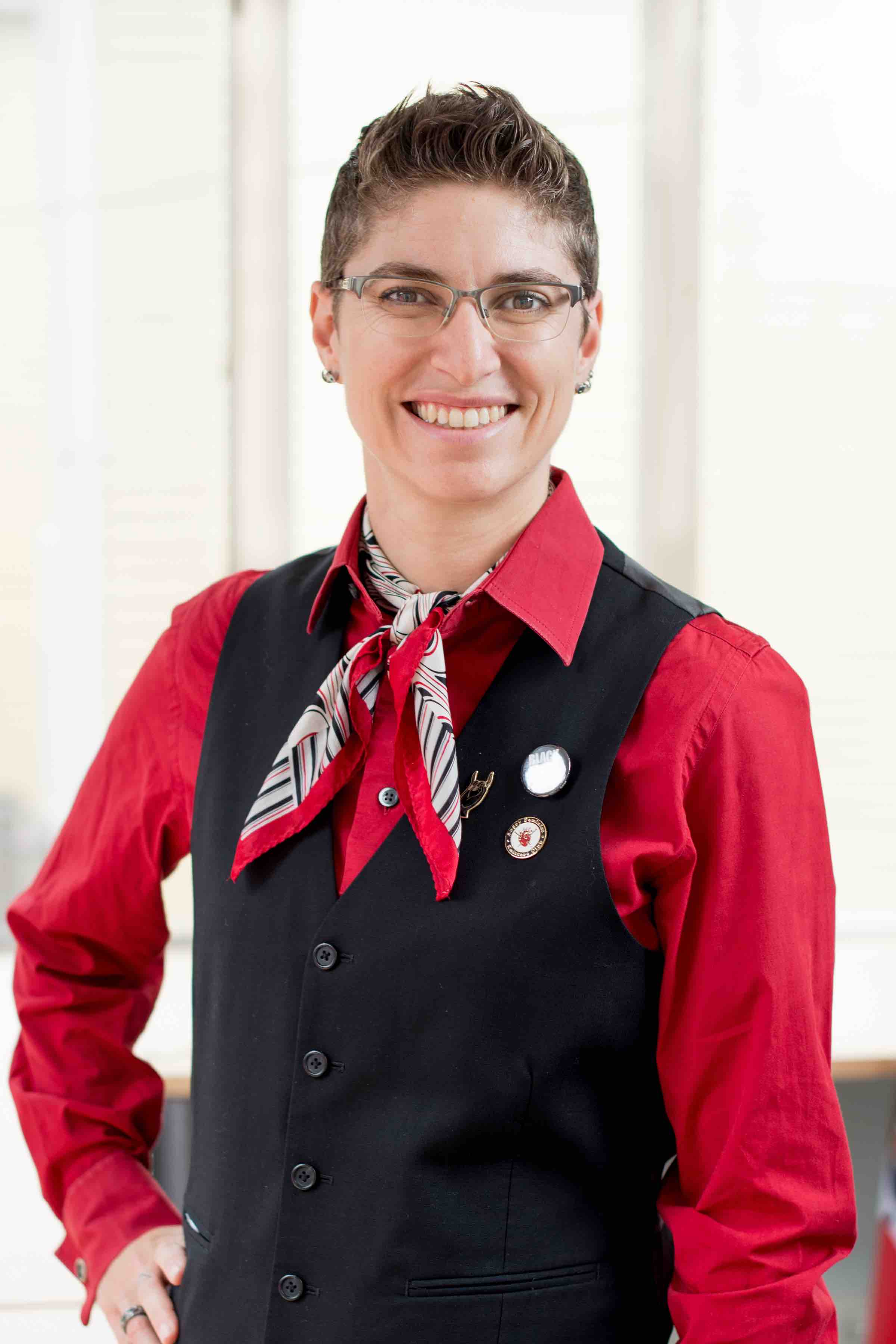 Jenn Steinfeld poses with a red shirt, black vest, and hand on hip