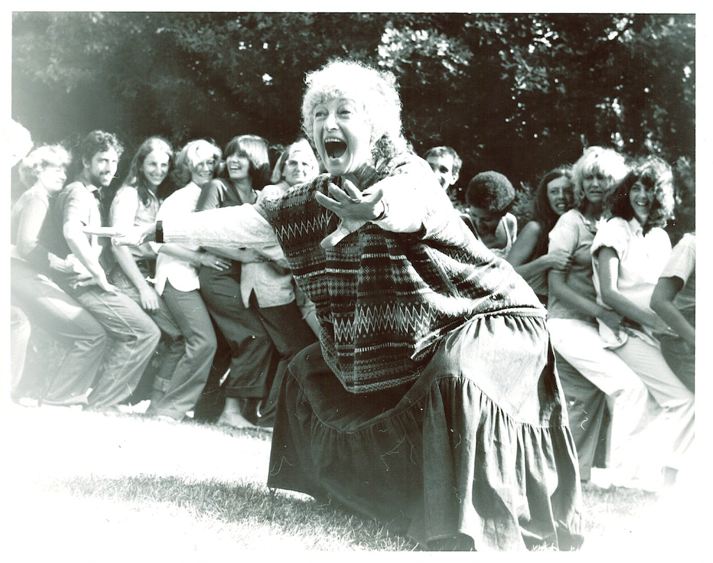 Black and white photo of woman dancing outside with line of dancers behind her.