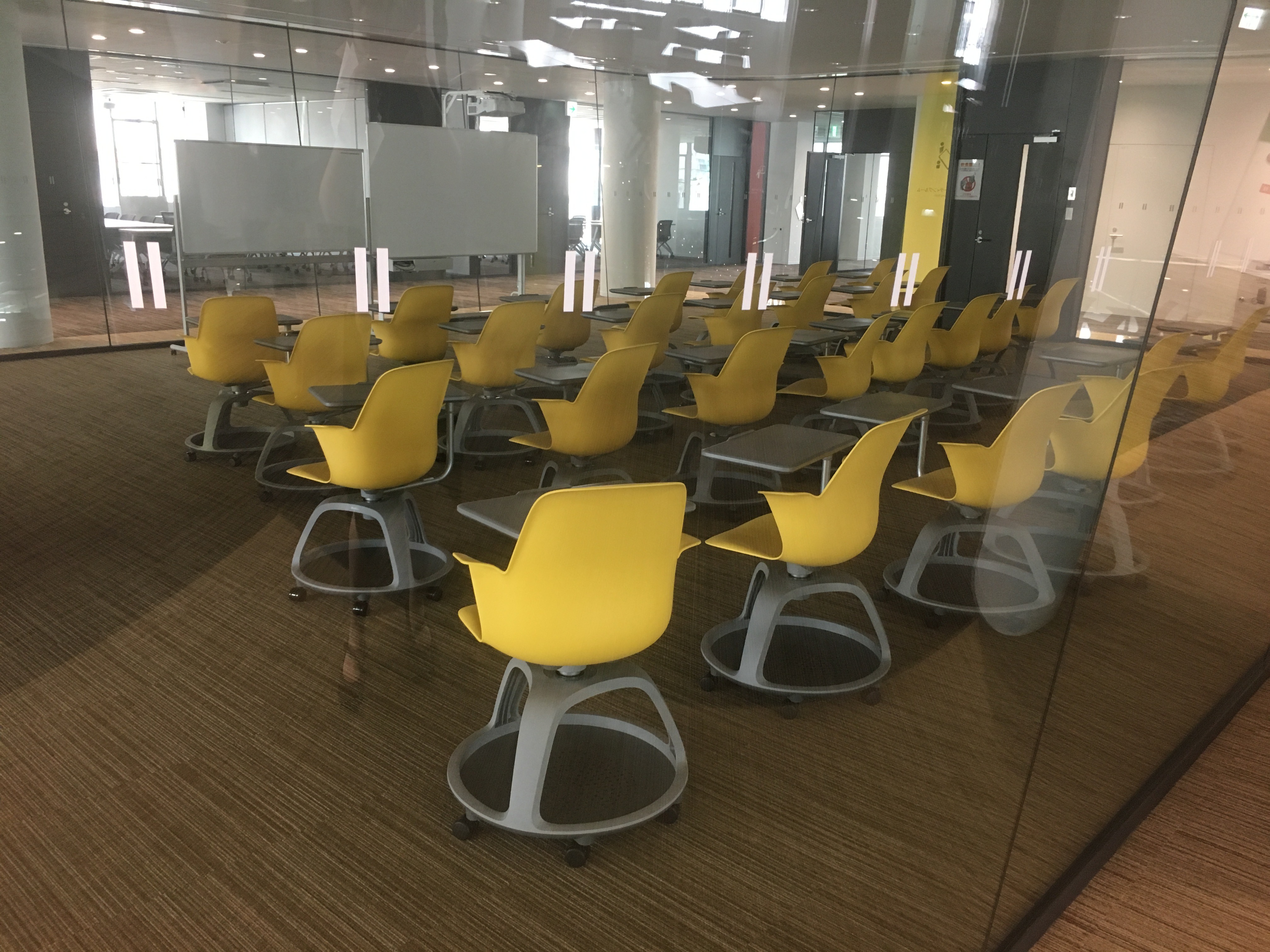 A classroom of yellow chairs that all have round trays attached underneath.