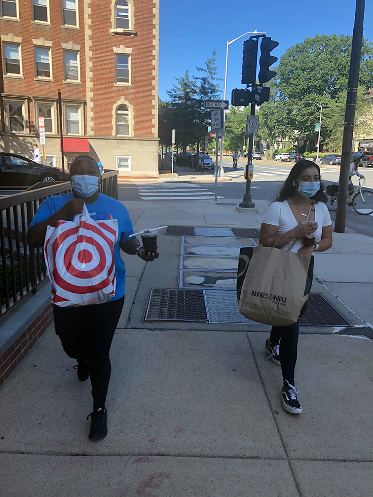 Demi Muhorakeye (left) and Stefani Osorio (right) pictured on a local shopping excursion. They are walking outside in Cambridge on a sunny day. Demi is holding a Target bag and a coffee and Stefani is holding a Barnes & Noble bag