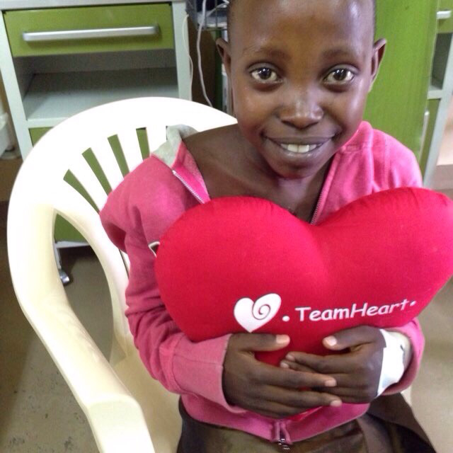 Demi Muhorakeye is pictured after her life-saving surgery in Rwanda. She is holding a heart-shaped pillow that says "TeamHeart"