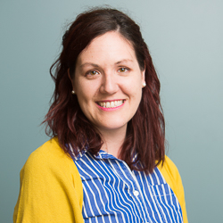 Headshot of Emily Earle wearing a blue shirt and a yellow cardigan.