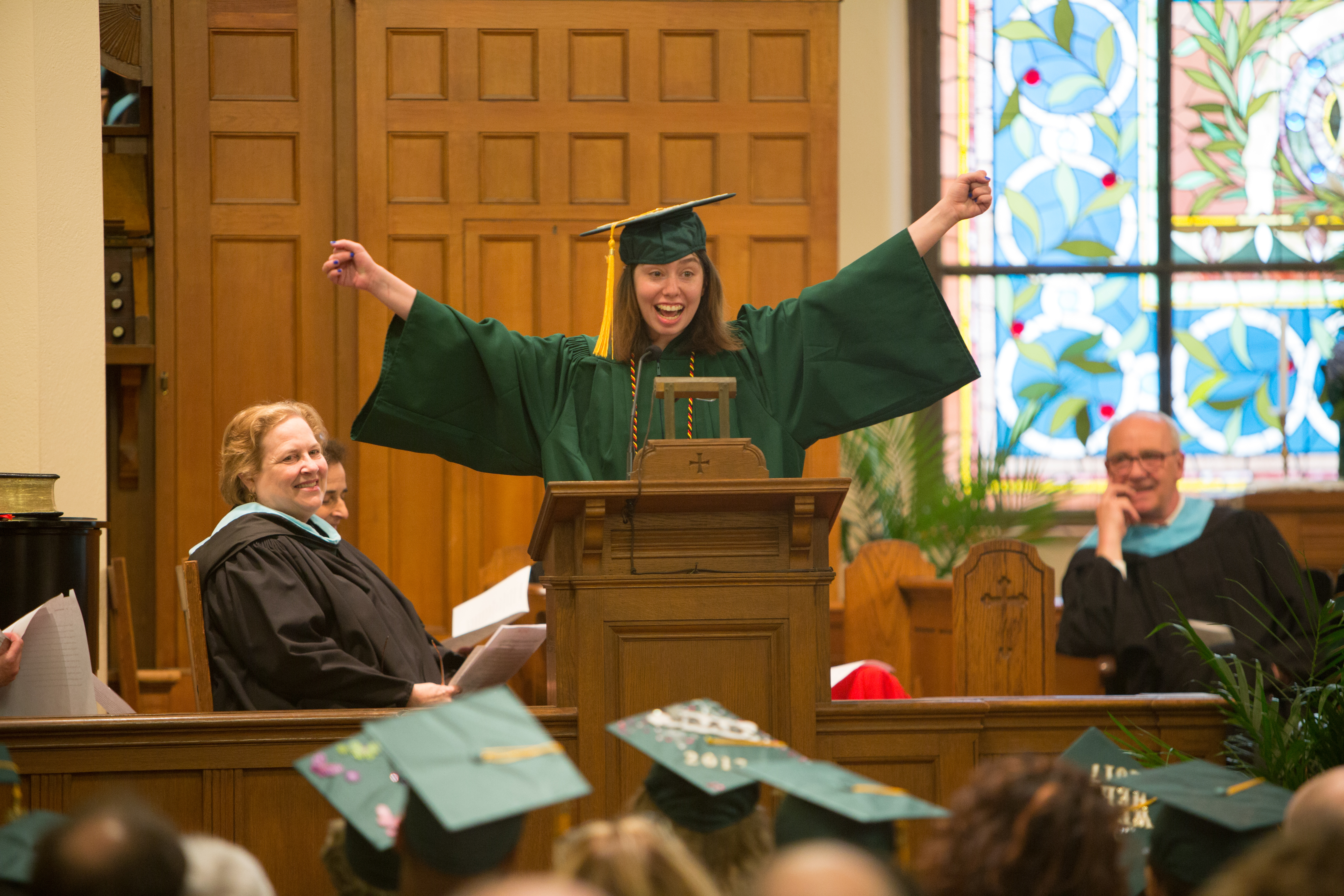 student speaker standing with arms in the air as she gives her speech at threshold graduation