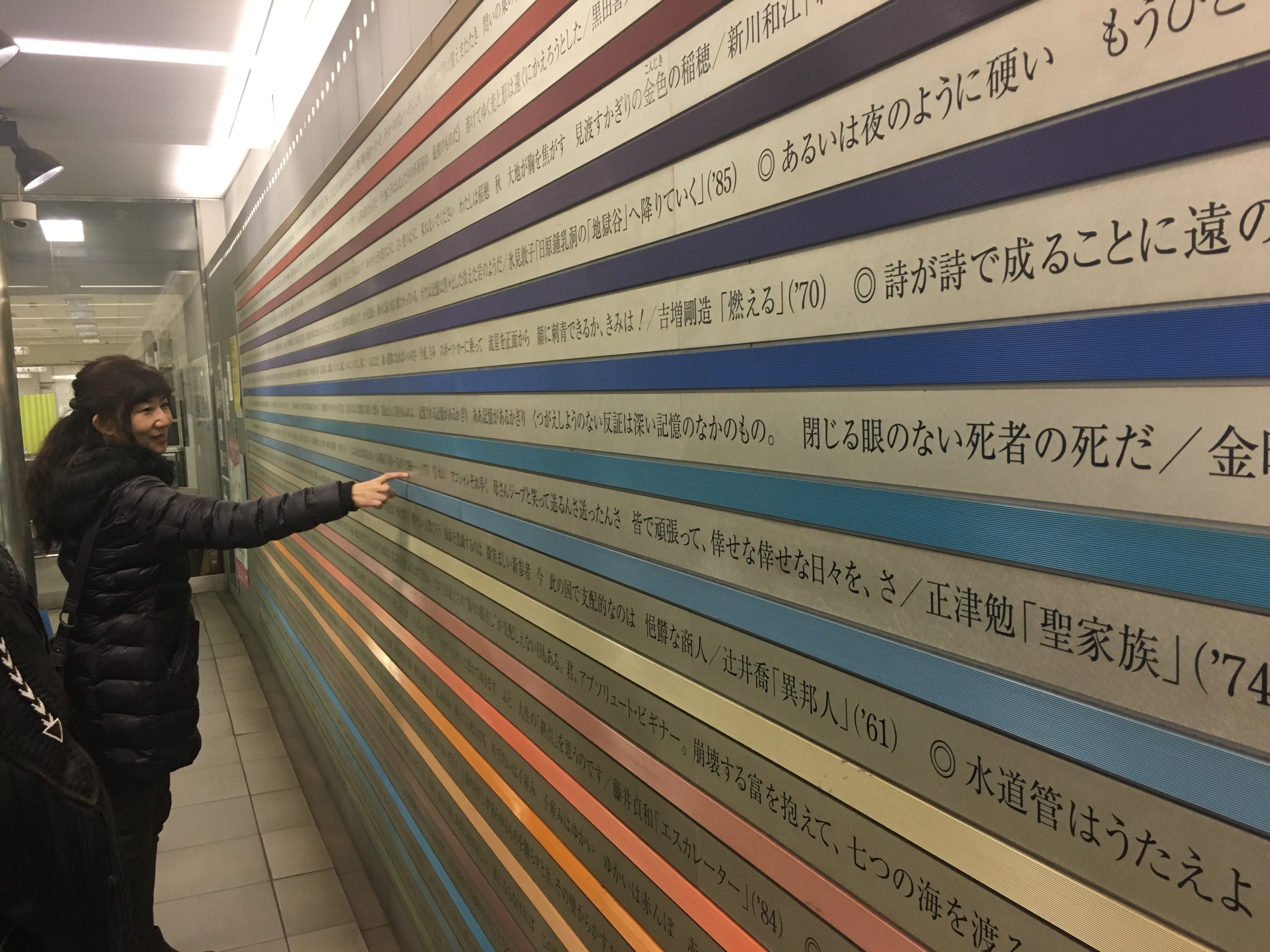 Professor Kazuyo Kubo looks at poetry printed on the walls of a subway station. Between each line is a band of color.