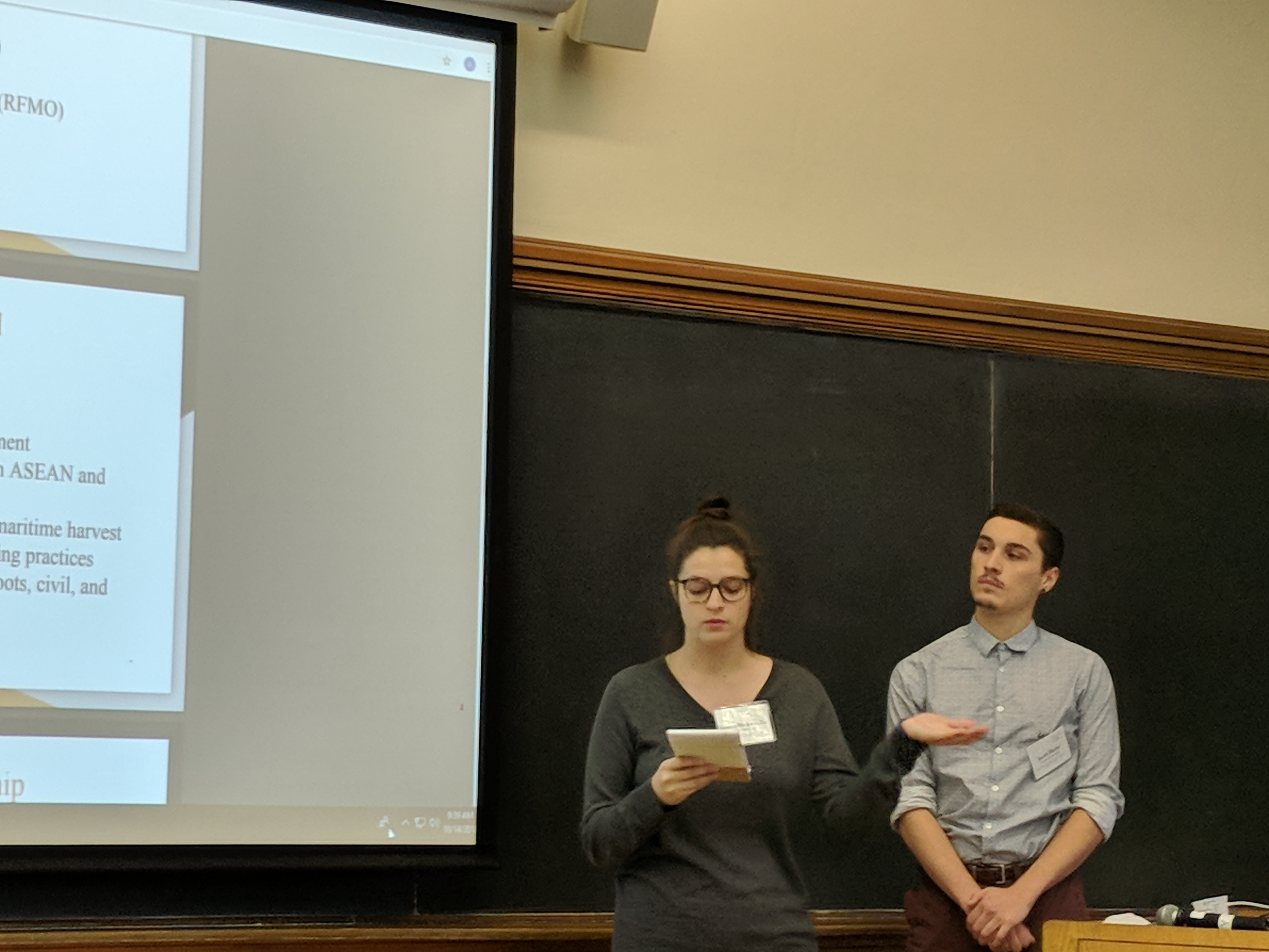 Students Kolette Bodenmiller and Jacob Hicks stand in front of a blackboard at Yale and present during the policy competition