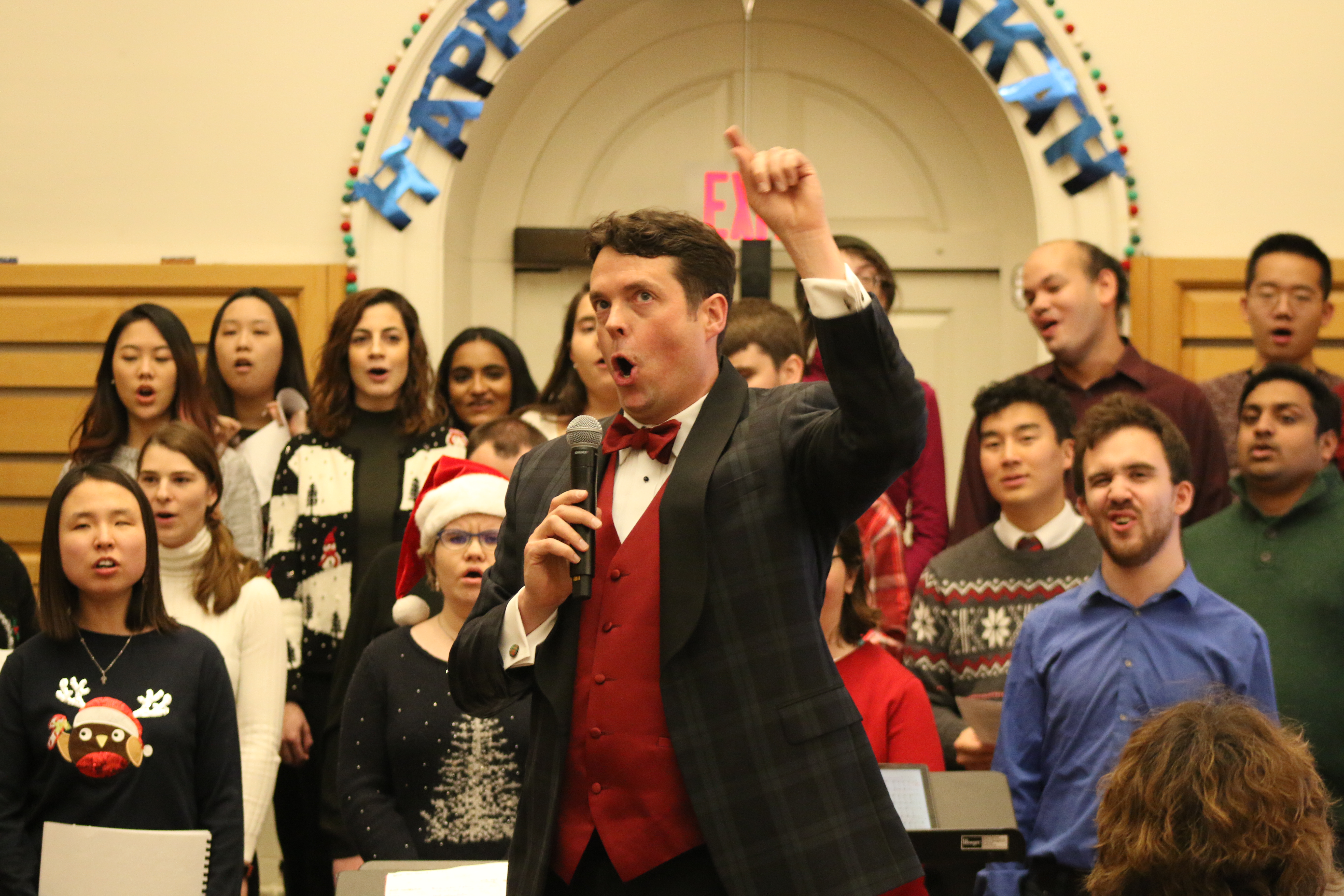 A man (the choir director) sings with hand raised at the holiday concert