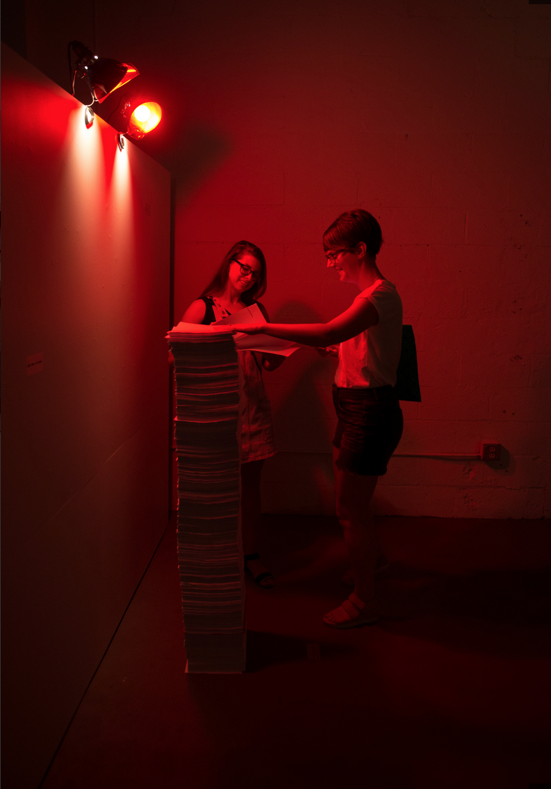 two people stand looking at huge stack of paper in dimly lit red room 