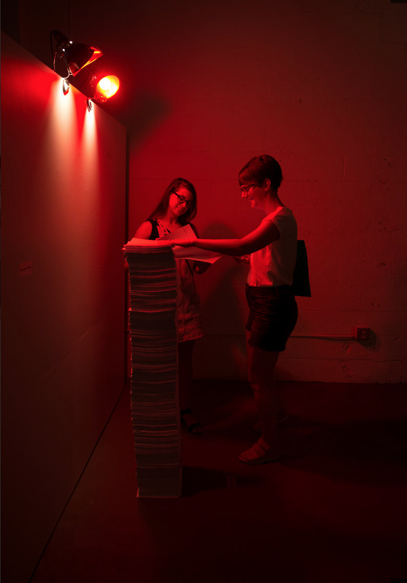 two people stand looking at huge stack of paper in dimly lit red room