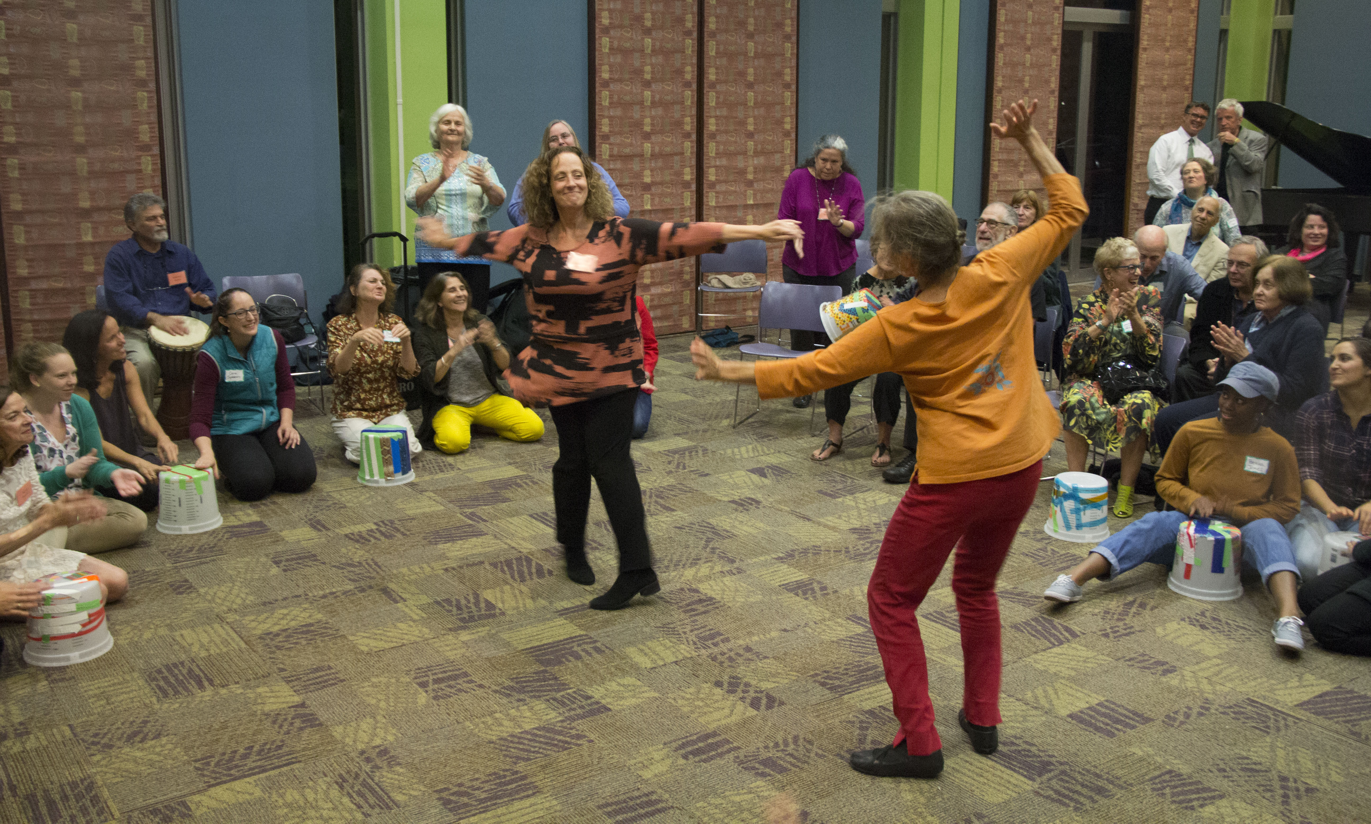 Two women dancing in the middle of a circle of people sitting down. 