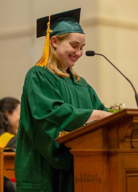 Olivia Gaffney smiles at the podium in her green graduation cap and gown