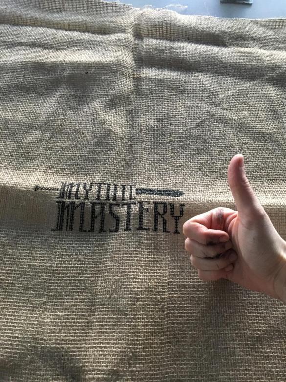 someone makes a "thumbs up" on a burlap bag with black text printed on it