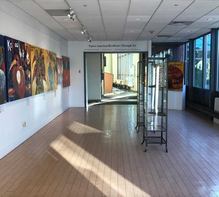view of gallery space with sun light coming through on floor and paintings hanging on the wall