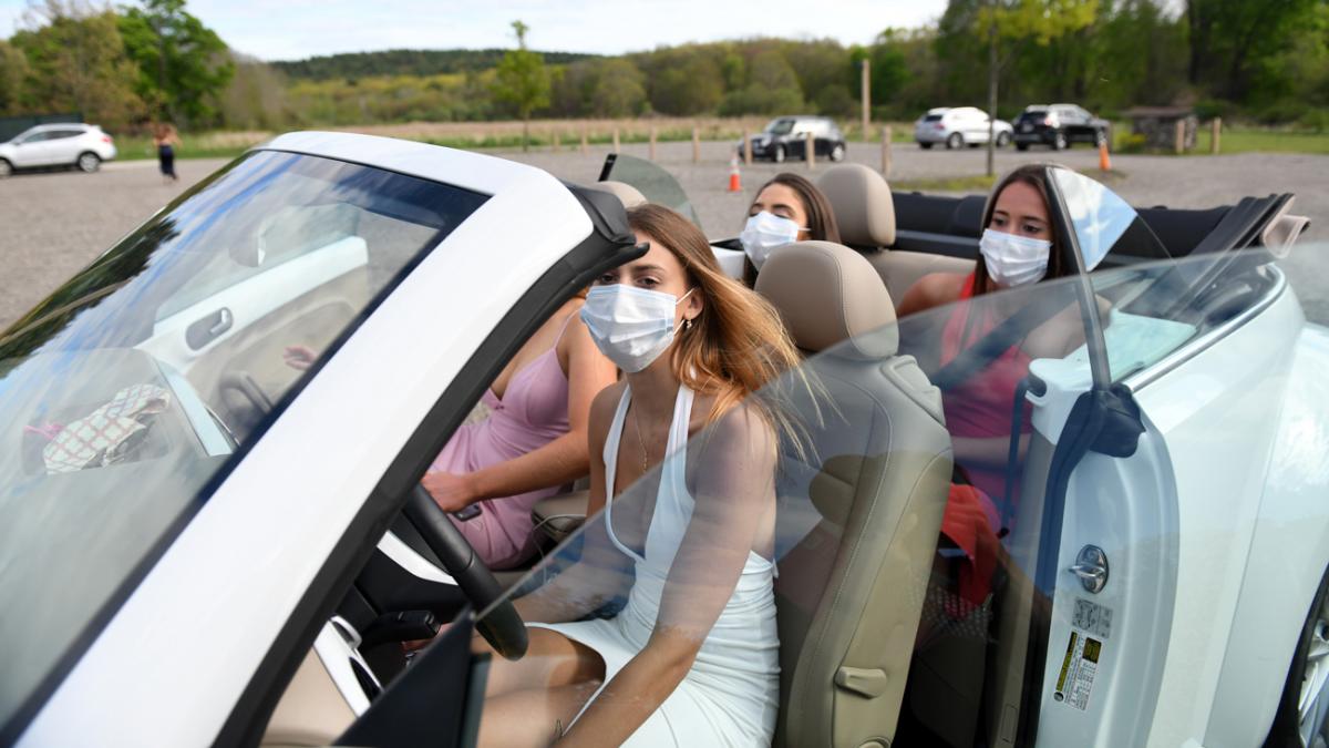 4 girls in a convertible with face masks on dressed up for the prom