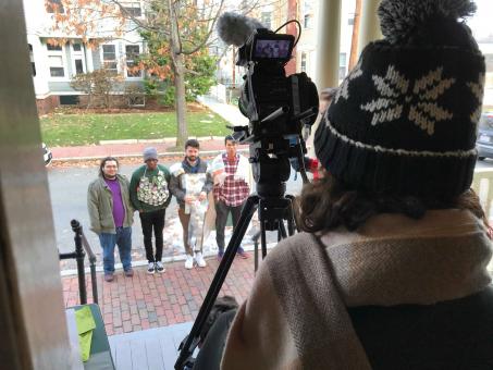 a picture of someone behind a video camera, filming four guys on a sidewalk wearing homemade armor.