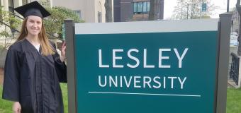 A photo of Alyssa Baumgarten in her cap and gown in front of the Lesley University sign at 1627 Massachusetts Ave. on Lesley's Doble campus. 
