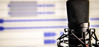 A microphone is in the foreground and a screen in the background.