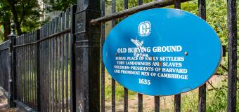 Blue plaque on the wrought iron cemetery fence reads: Old Burying Ground. Burial place of early settlers, tory landowners and slaves, soldiers, presidents of Harvard and prominent men of Cambridge.