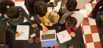 overhead view of children and teacher at table working with laptop and notebooks