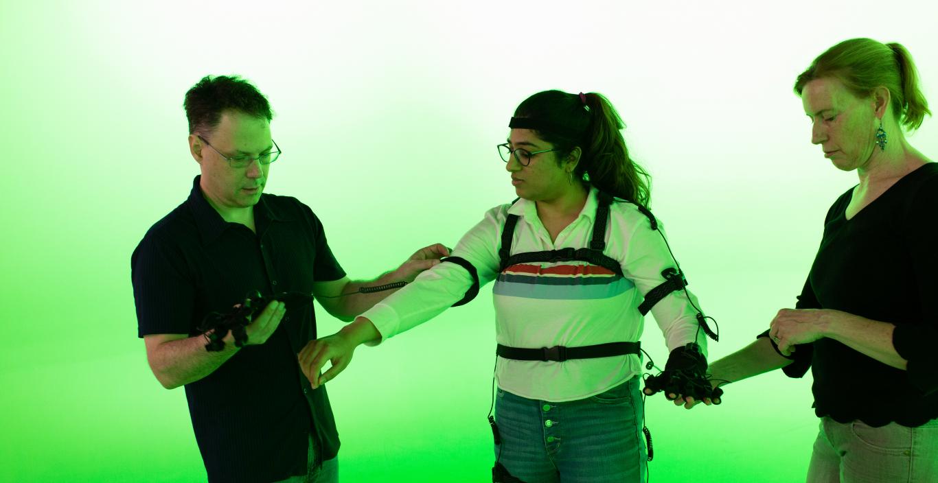 student trying out the motion capture suit in the green room with two faculty