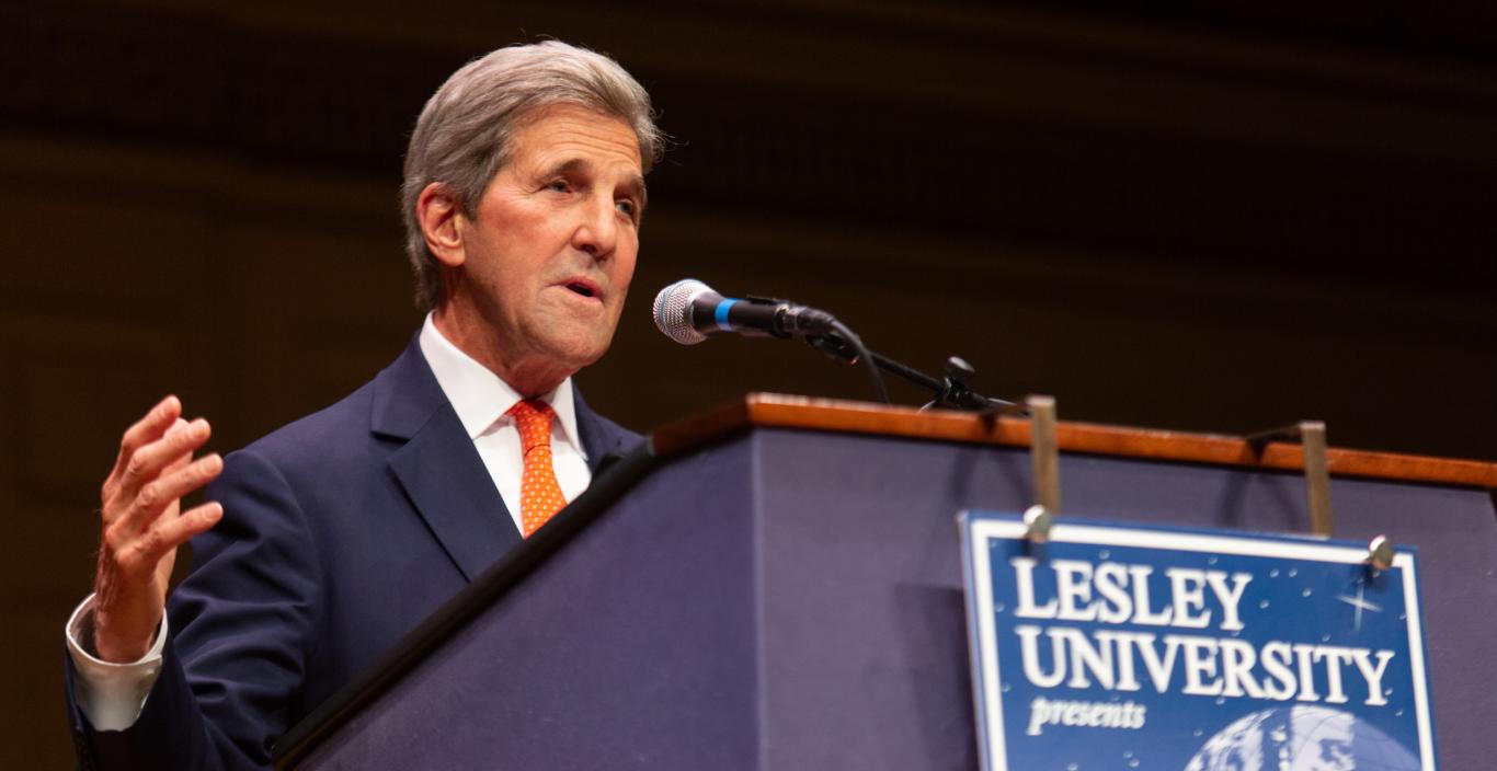 John Kerry speaks in front of a podium while gesturing with his right hand