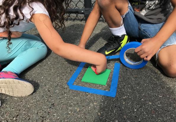 Children on sidewalk using colored tape to make shapes