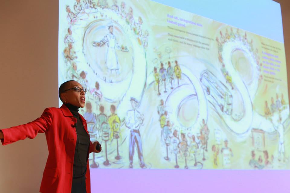 Andrea Pickney speaking in front of a projection of a page of her children's book