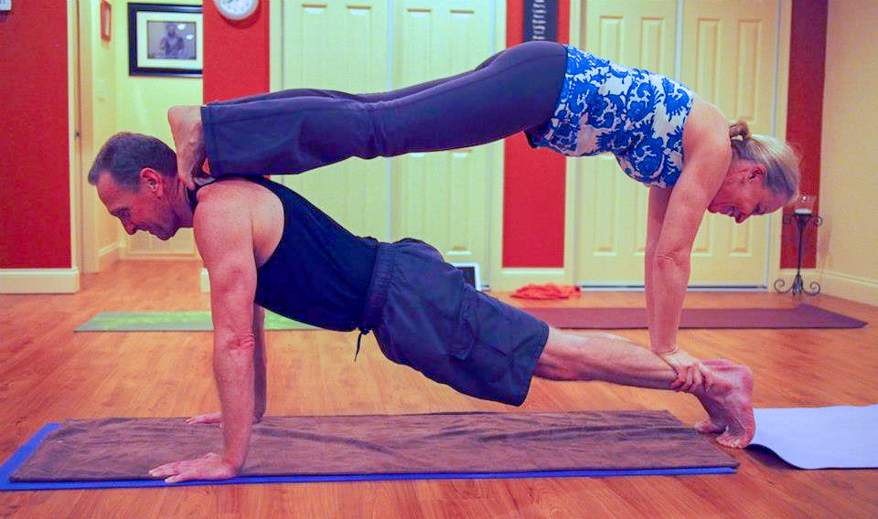Anusia Hirsch and her husabnd are in a yoga double plank with her feet on his shoulders.