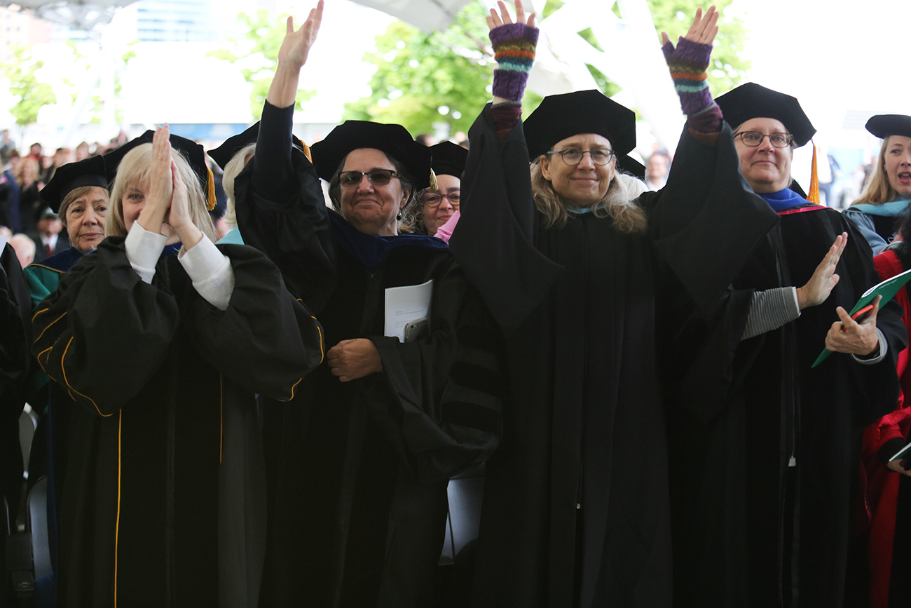 Faculty clap and raise their hands in celebration at Commencement.