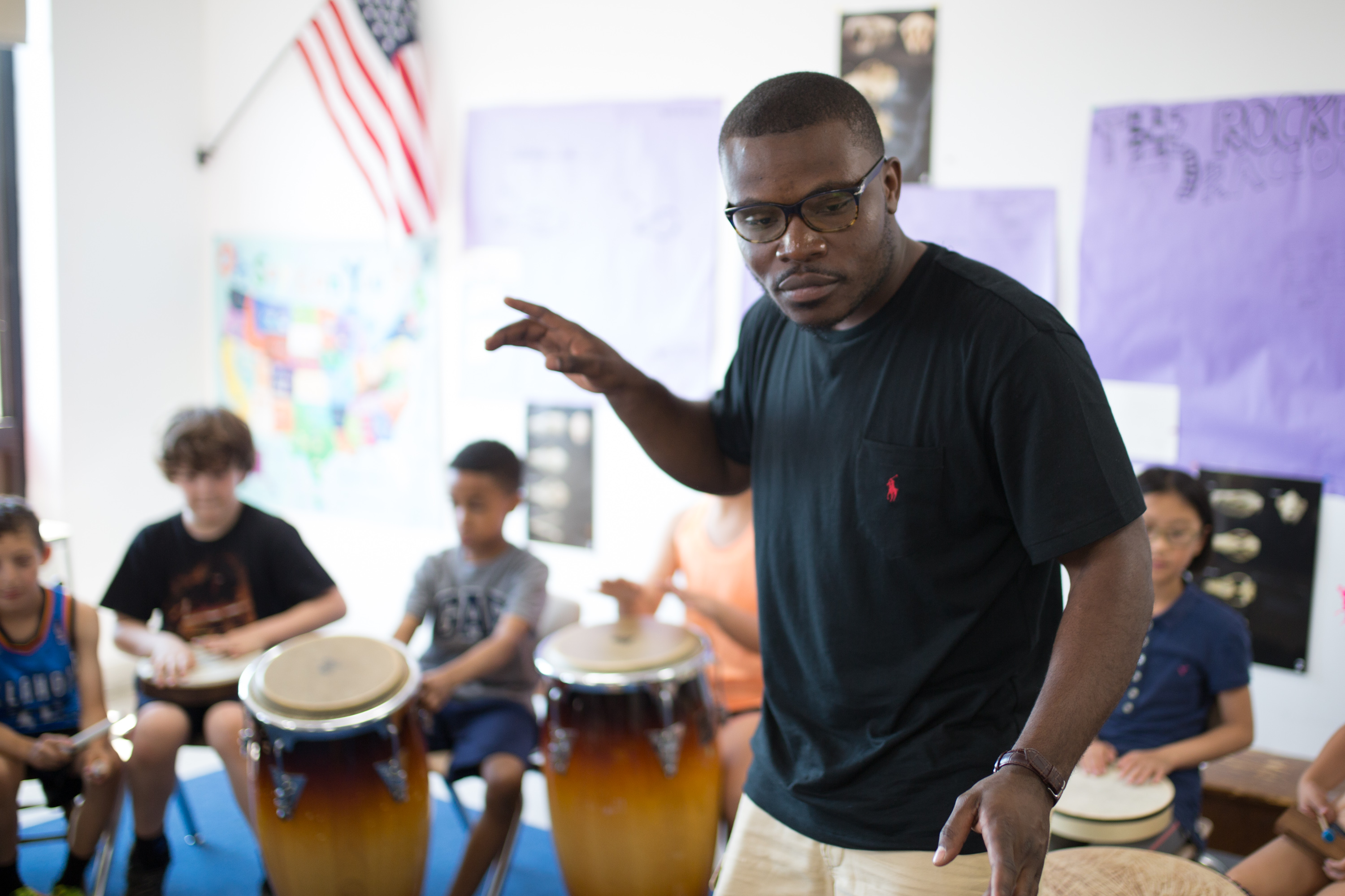 Jonathan Mande teaching a drum class with young children in a circle around him, each child holding a drum
