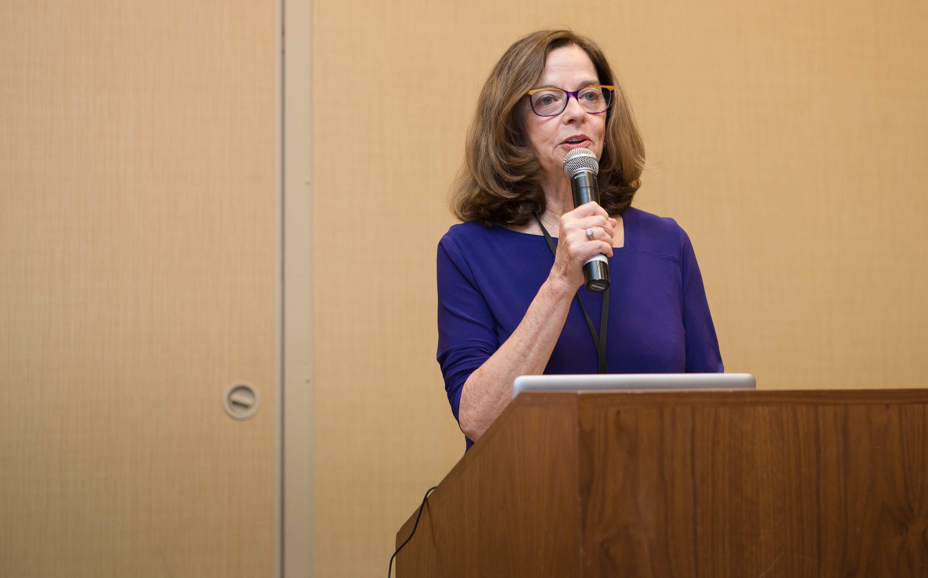 Nancy Beardall wearing a purple top speaks at a podium.