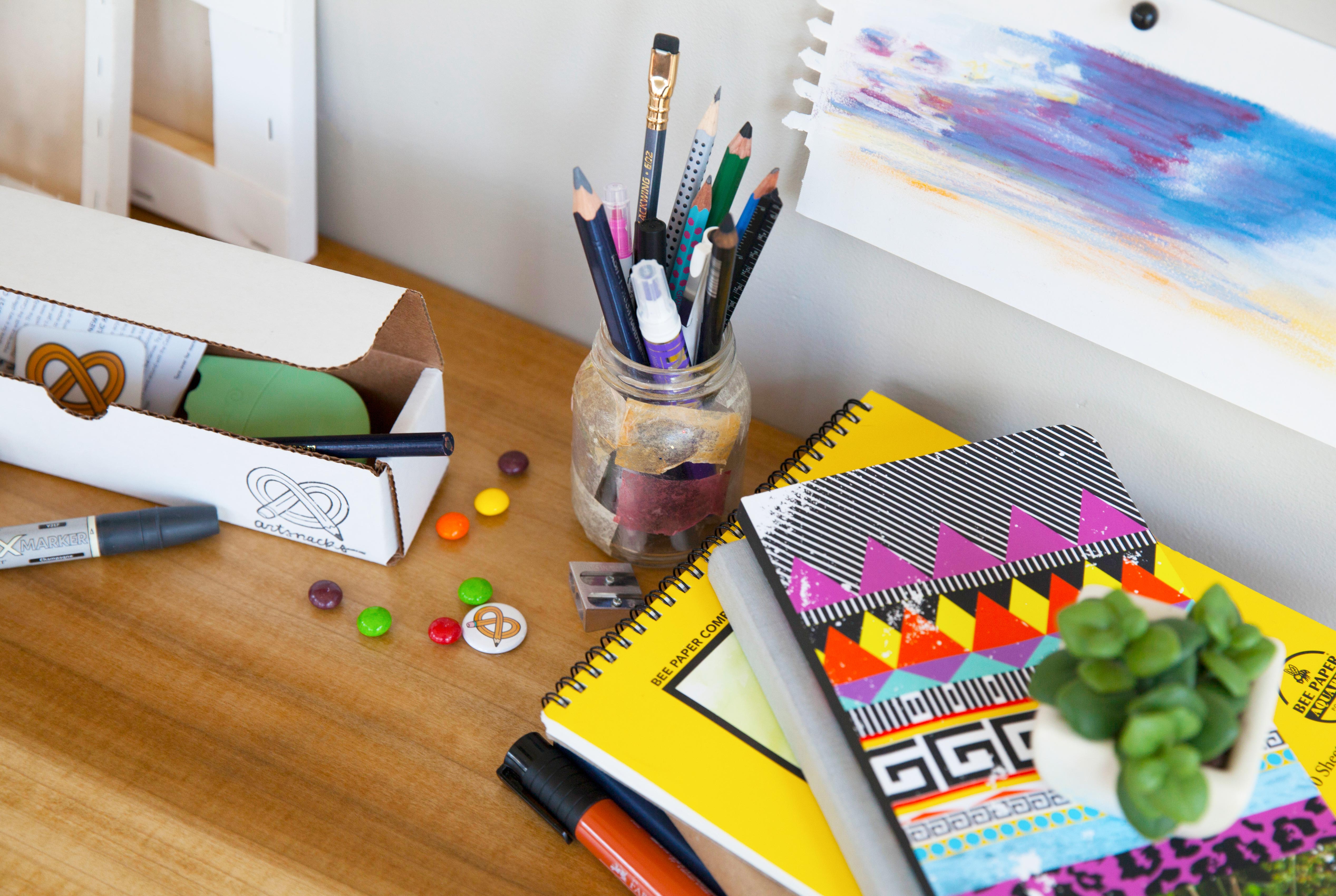 an open box from ArtSnacks sits on a desk next to books and paper