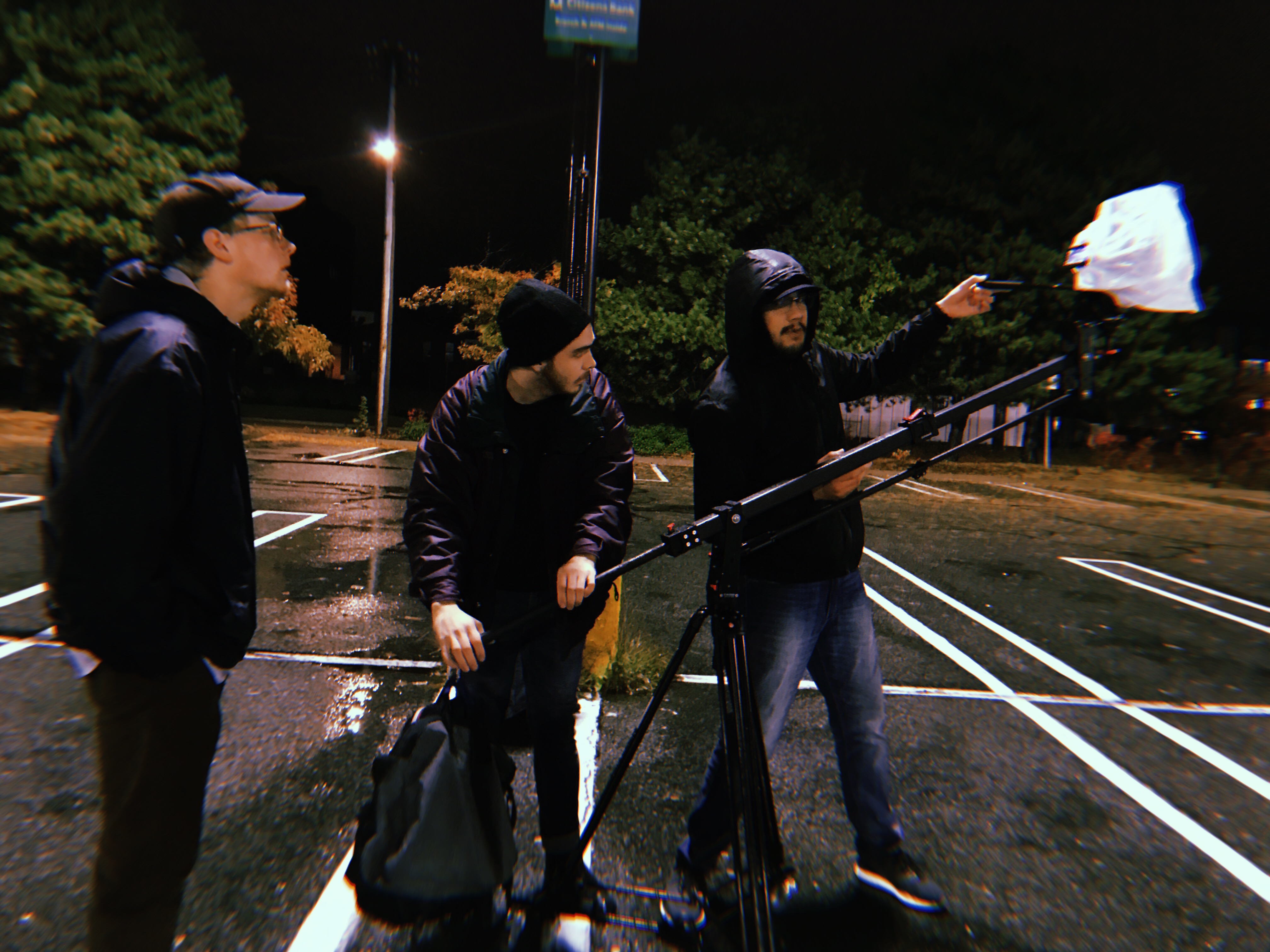 three film students set up a camera to record in an empty parking lot at night in the rain