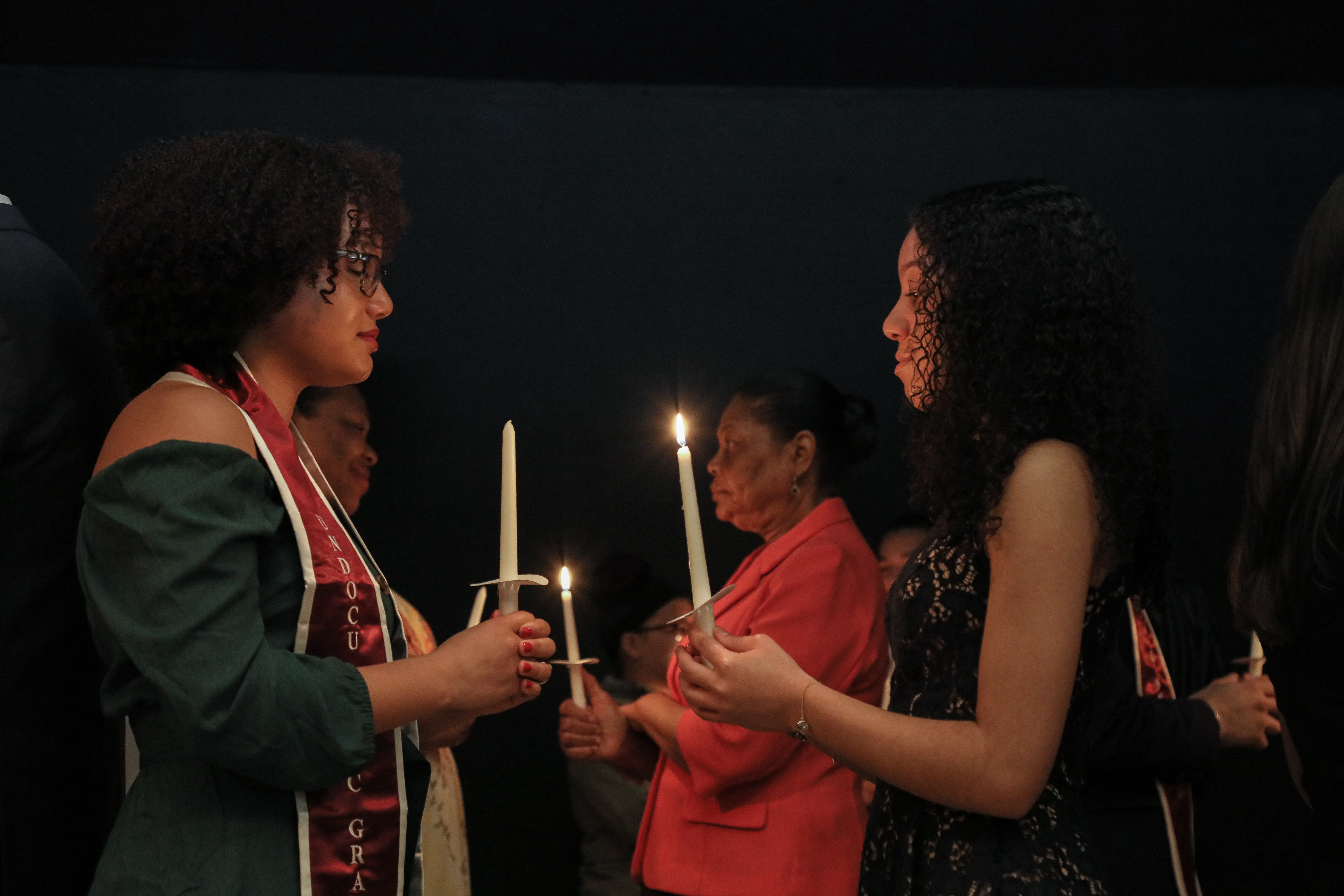 Women stand facing each other on the stage with lit candles.