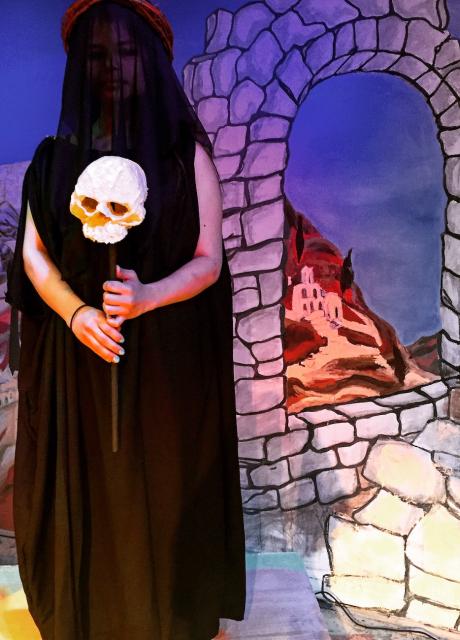 student acting in a play holding a skull wearing a cloak in front of a stone wall