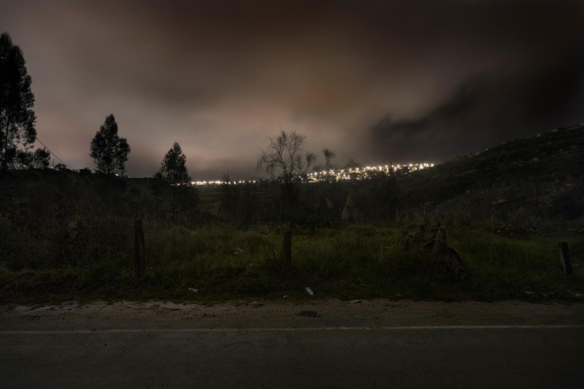 photograph of dark field with city lights in valley below