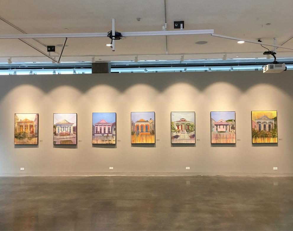 gallery photo with paintings of houses all lined up under spotlights. 