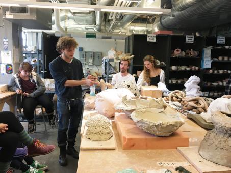 students sit around large studio table discussing clay sculpture work