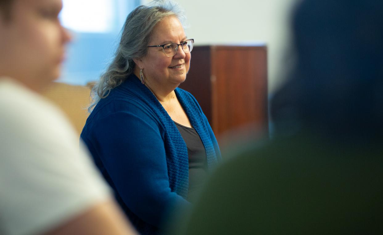 Woman with glasses and a blue sweater seated and speaking to a crowd of students