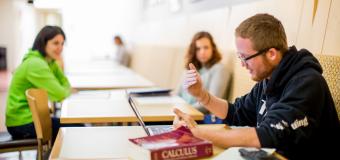 three students sit at tables with a calculus textbook and calculator