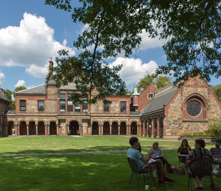 Students sit in chairs in a circle having a class discussion on Lesley's lawn.