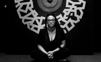 Ya La'Ford sits in front of a mural, photo in black and white.