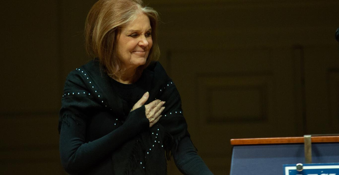 Gloria Steinem laying her hand across her chest in a gesture of gratitude