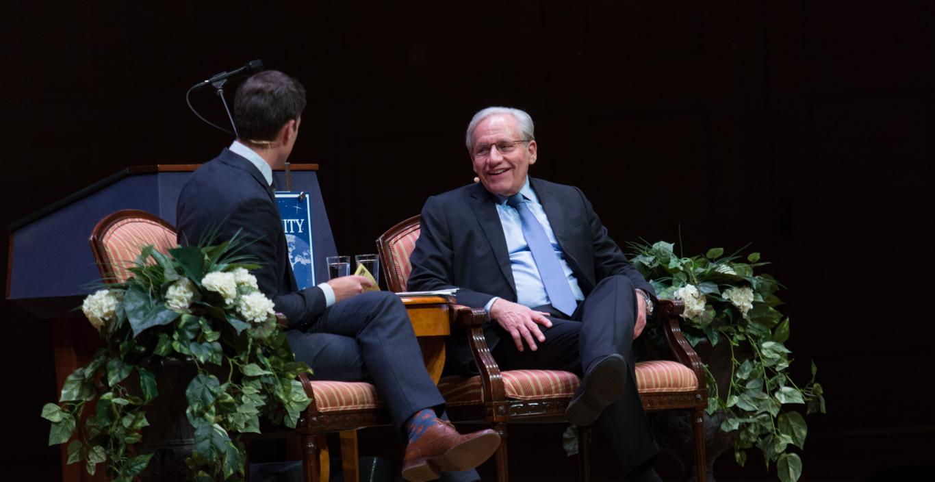 two men sitting on a stage in conversation for an interview