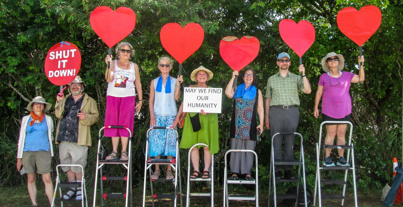 Group of people standing on step stools outside holding up red heart cutouts