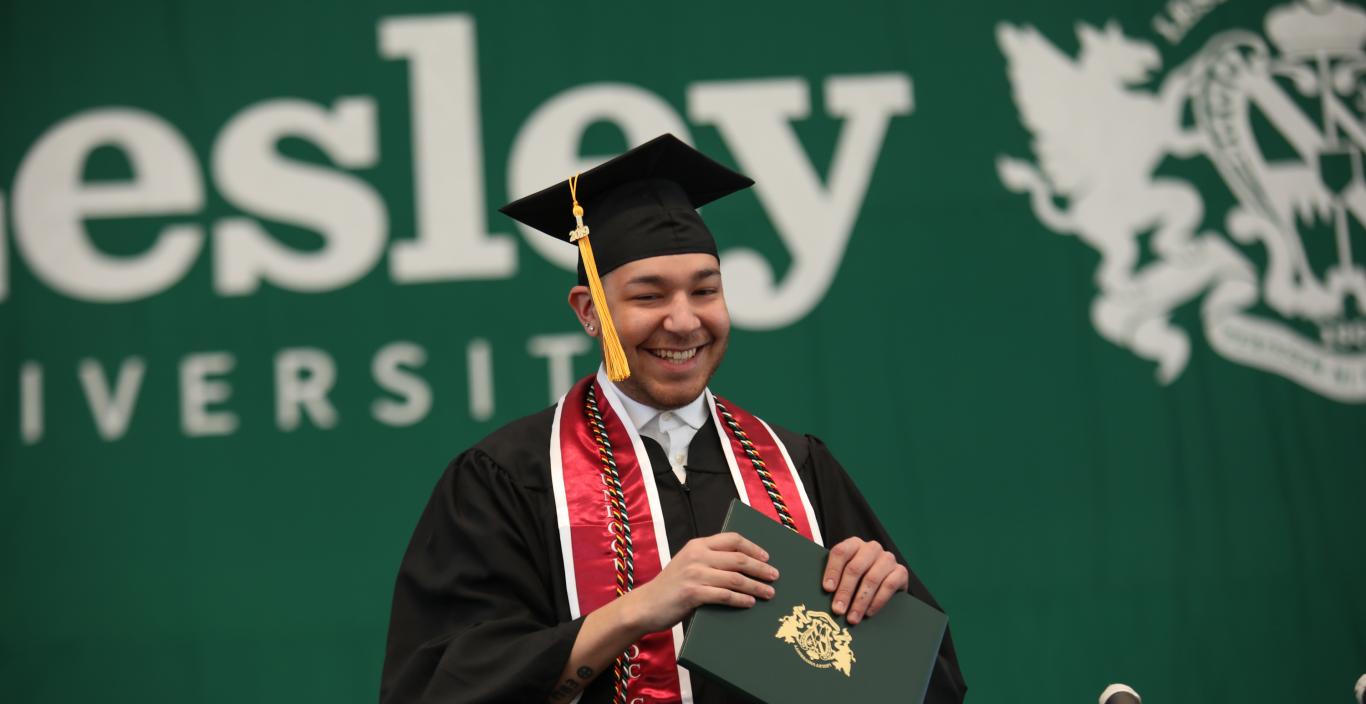 Young man walking across the stage with his diploma at Lesley Commencement in 2019.