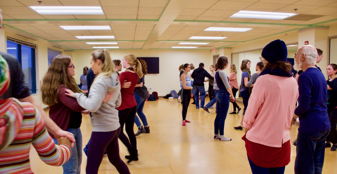 Professor watches as students dance in swing dance class in dance studio.