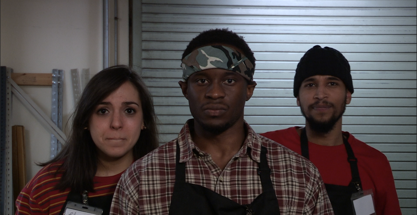 Three people wearing black aprons look into the camera 