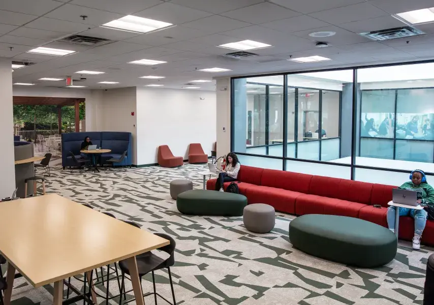 An open room with large windows, couches, chairs, and a table with several students working